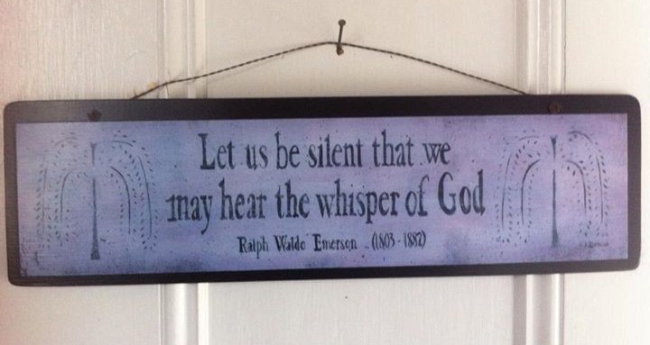 Wooden sign on a white door that leads into the Worship area of the meetinghouse. The sign reads: "Let us be silent that we may hear the whisper of God". Underneath the text, it reads: "Ralph Waldo Emerson (1803-1887)".